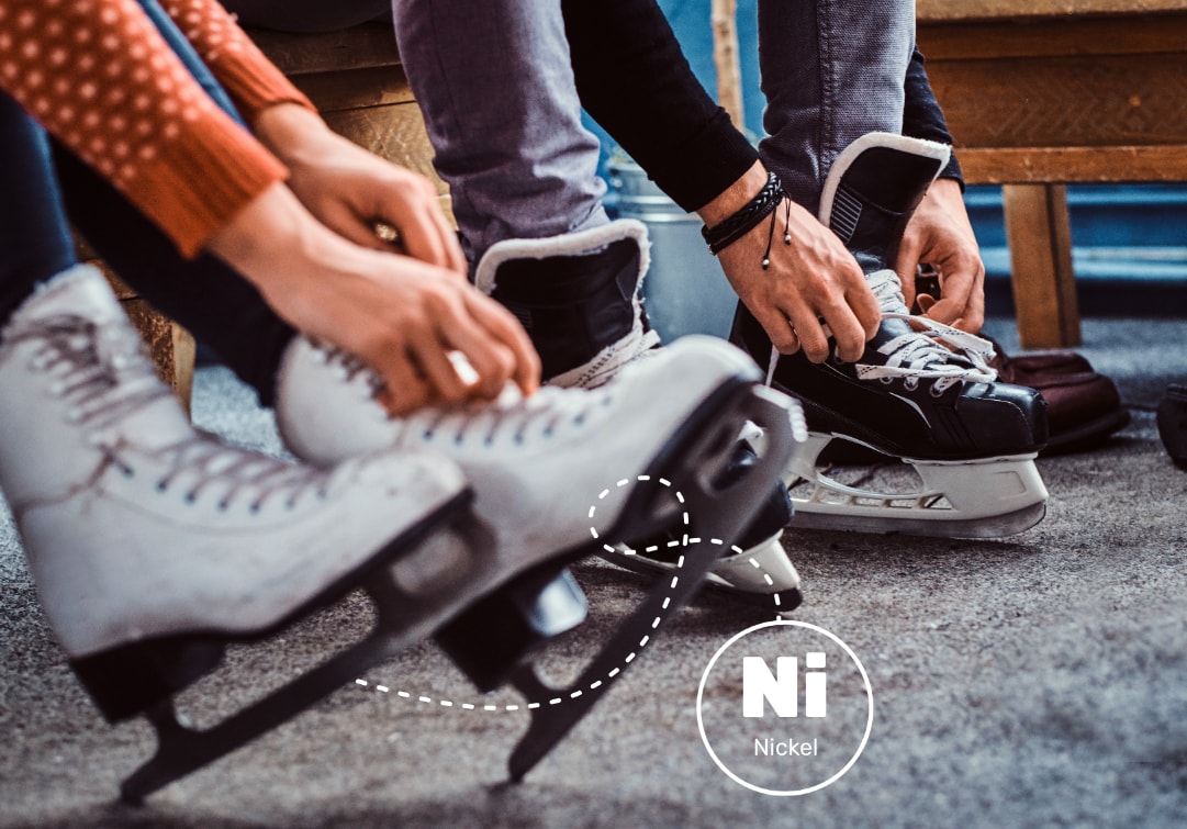 Image of two individuals tying the laces of ice skates. Only their feet, legs and hands are visible. Nickel is used in skate blades.